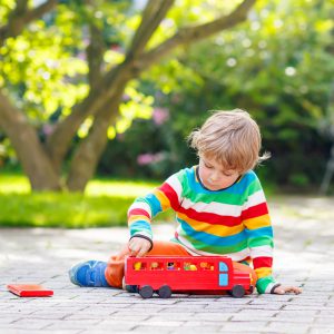 niño juega en el suelo de un jardin con un autobus de juguete