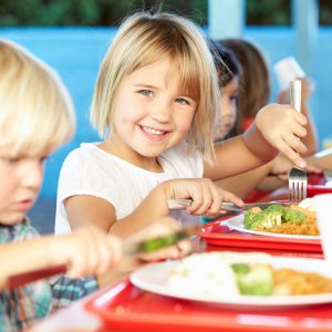 niña sonrie en el comedor escolar mientras almuerza