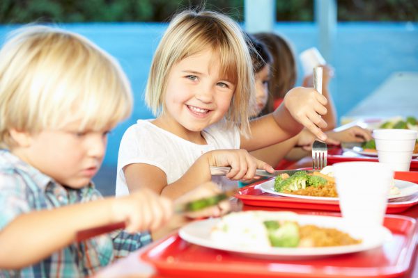 niña sonrie en el comedor escolar mientras almuerza