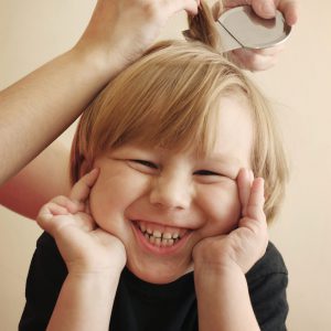 niño sonrie mientras le pasan la liendrera por el pelo