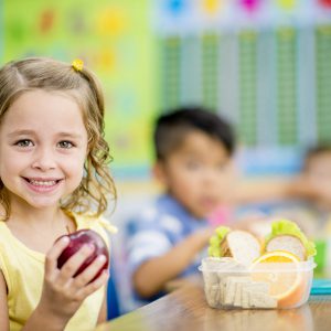 niña sonrie con una manzana en la mano