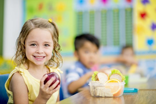 niña sonrie con una manzana en la mano