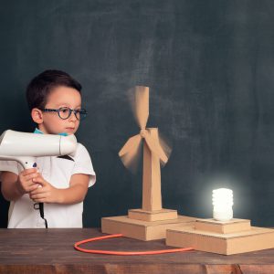 niño hace girar una maquesta de un aereogenerador de cartón con un secador de pelo.