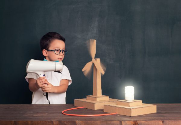 niño hace girar una maquesta de un aereogenerador de cartón con un secador de pelo.